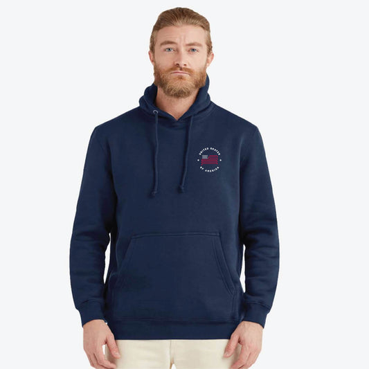 A man wearing a navy blue pullover hoodie with a small United Skates of America circular chest graphic, paired with light beige pants, photographed against a solid light gray background.