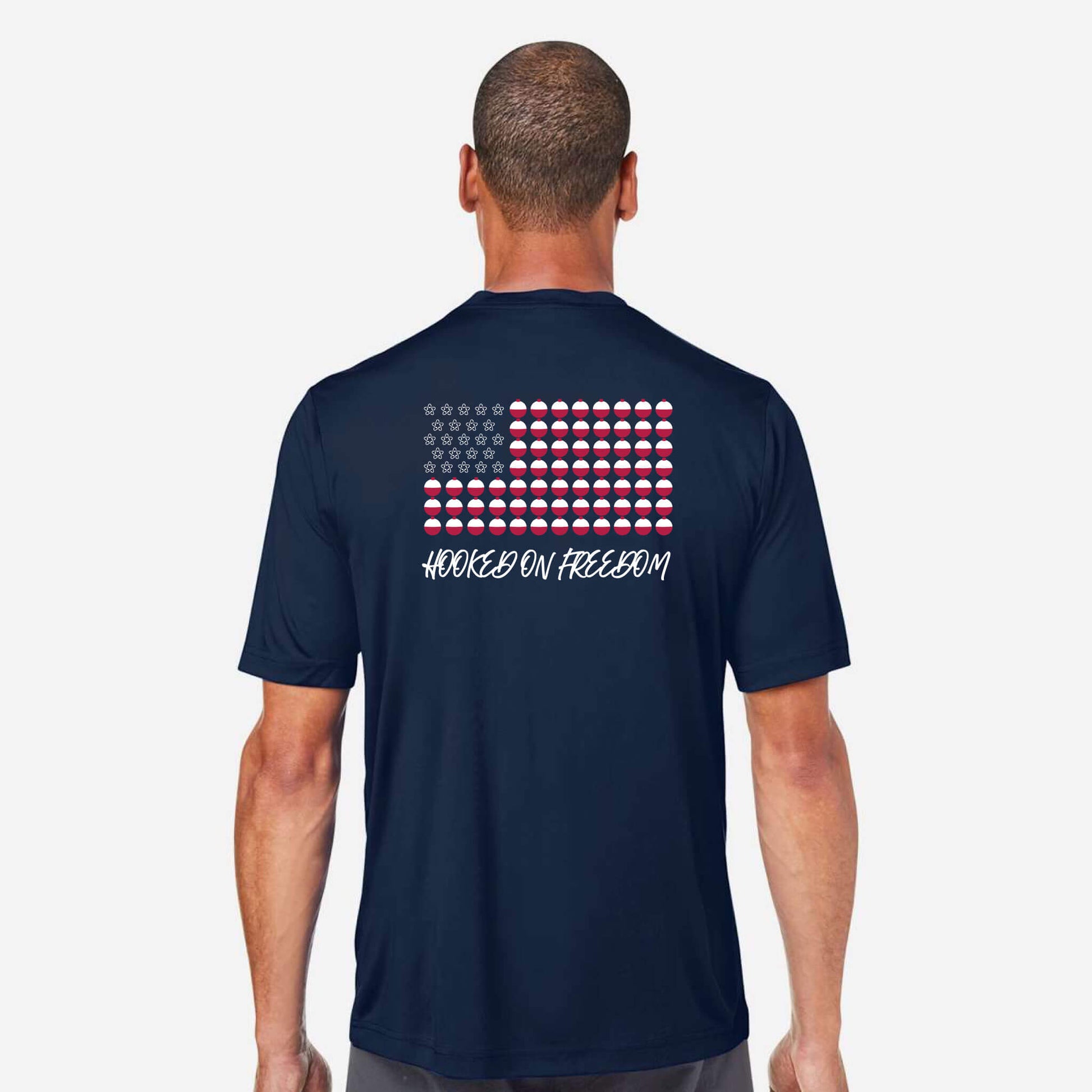 A man viewed from the back wearing a navy blue t-shirt with a graphic of a stylized American flag made of red, white, and blue flags, with the text 'HOOKED ON FREEDOM' printed below it.