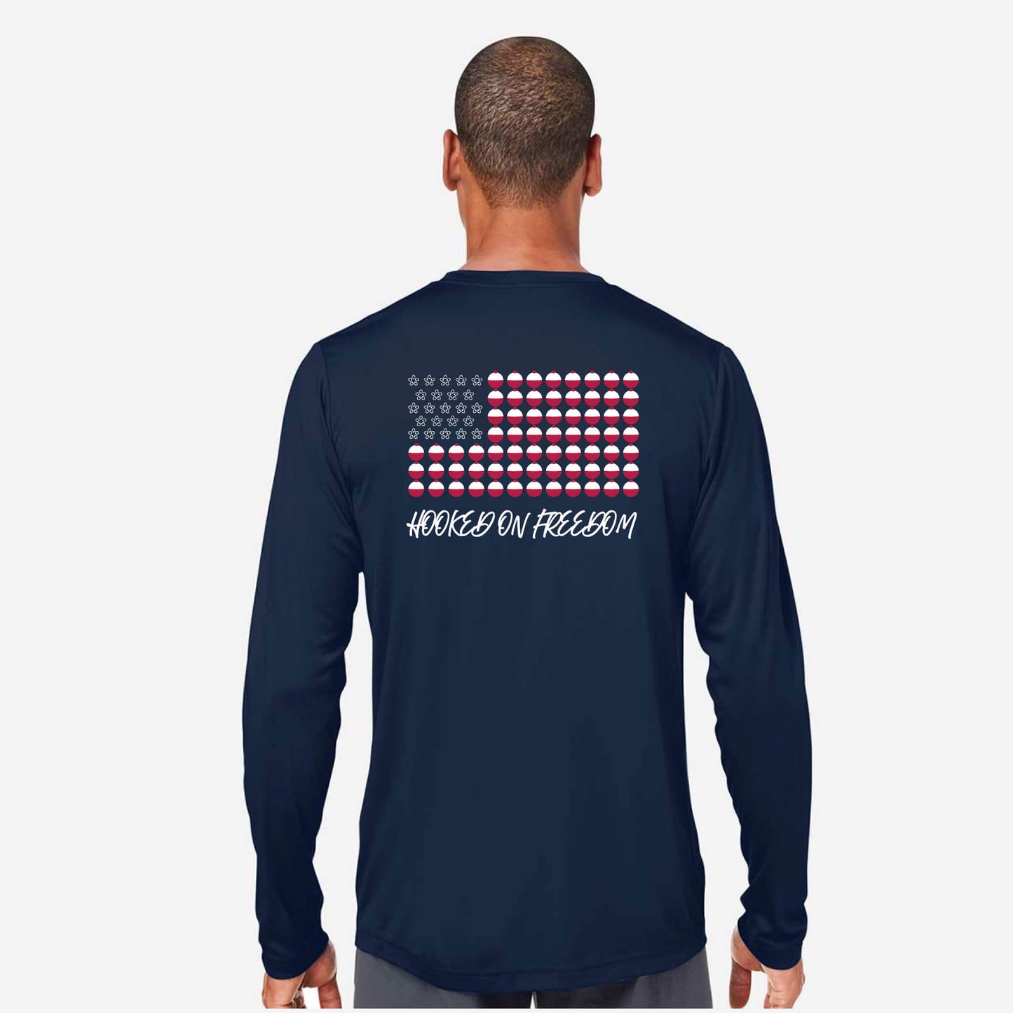A man viewed from the back wearing a navy long-sleeve shirt with a patriotic graphic on the back. The graphic features a stylized American flag made of red, white, and blue pucks, with the text 'HOOKED ON FREEDOM' printed below in white.