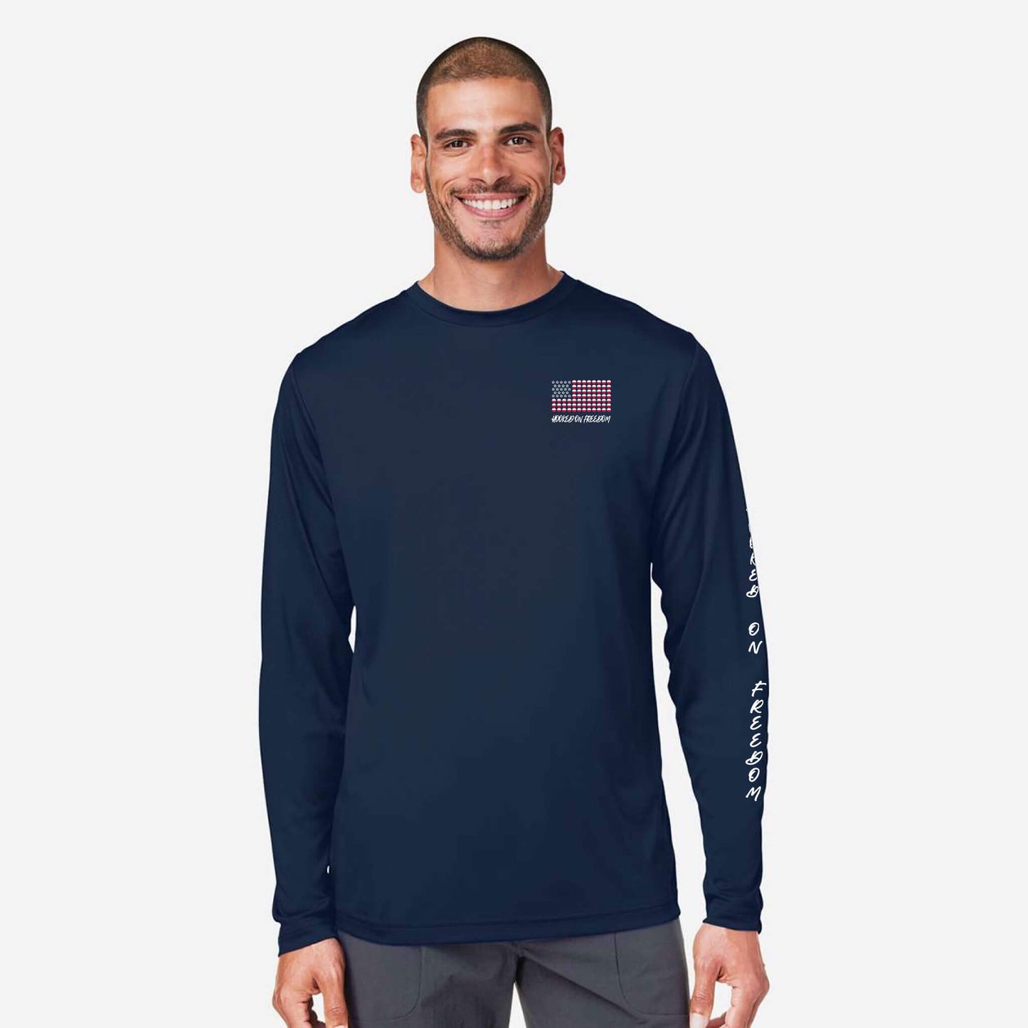 A man wearing a navy blue long-sleeve performance shirt with a small red, white, and blue American flag graphic on the left chest and white text down the right sleeve, set against a light gray background.