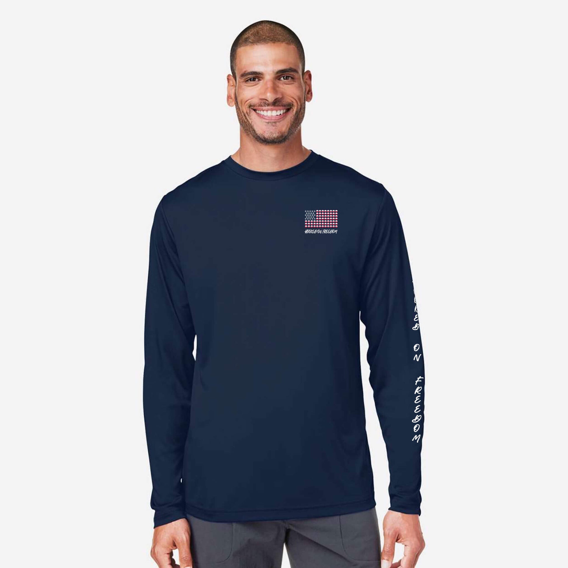 A man wearing a navy blue long-sleeve performance shirt with a small red, white, and blue American flag graphic on the left chest and white text down the right sleeve, set against a light gray background.