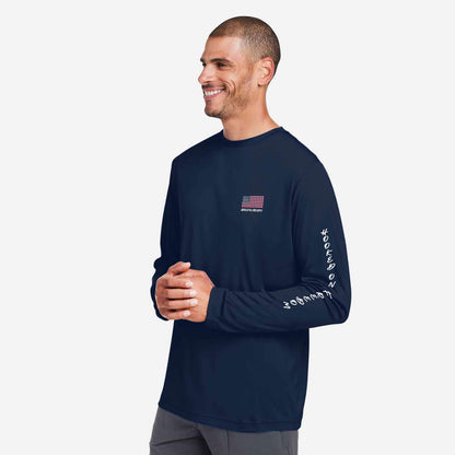 A man wearing a navy blue long-sleeve performance shirt with a small American flag logo on the left chest and white script text down the right sleeve, photographed against a light gray studio background.