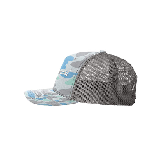 A trucker-style baseball cap with a gray mesh back and a camouflage-patterned front panel and brim. The pattern features shades of gray, light blue, and white, with a script logo on the side.