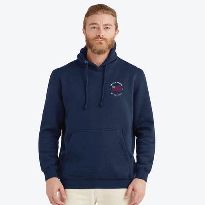 A man wearing a navy blue pullover hoodie with a small United Skates of America circular chest graphic, paired with light beige pants, photographed against a solid light gray background.